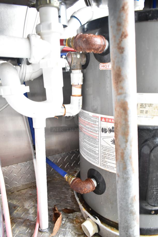 Mobile kitchen trailer interior showing pipes and heater with rust; labels warn of hot surface and provide safety info.