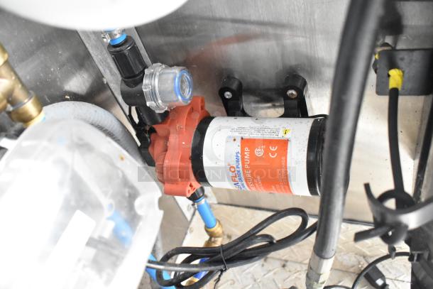 Inside view of mobile kitchen trailer featuring a Flojet pump system. Shows hose connections and wiring details.