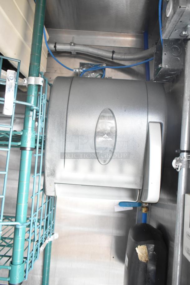 Mobile kitchen trailer interior with stainless steel surfaces, green wire shelving, and a Georgia-Pacific dispenser.