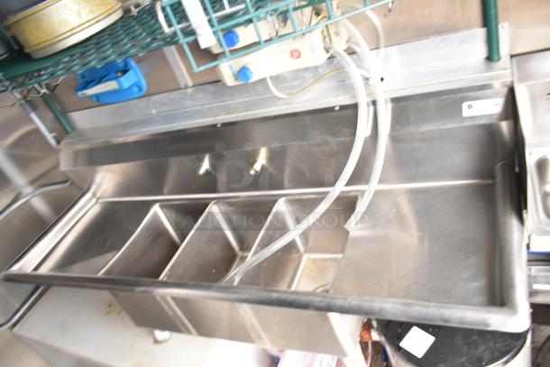 Mobile kitchen trailer interior featuring a stainless steel sink, with pipes and a shelving unit above.