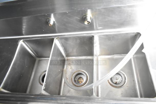Stainless steel sink in mobile kitchen trailer, featuring multiple basins. Slight wear visible, ideal for food prep.