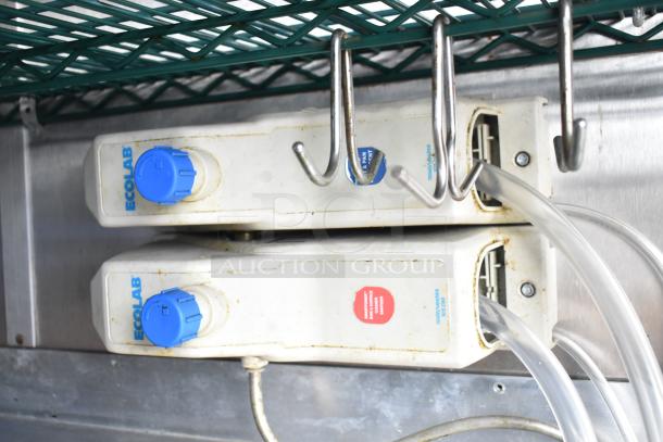 Mobile kitchen trailer interior with Ecolab soap dispensers, blue knobs, metal hooks, and tubing on a metal shelf.
