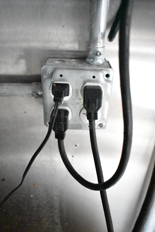 Power outlet with multiple black cords plugged in, indicating electrical connectivity in mobile kitchen trailer.