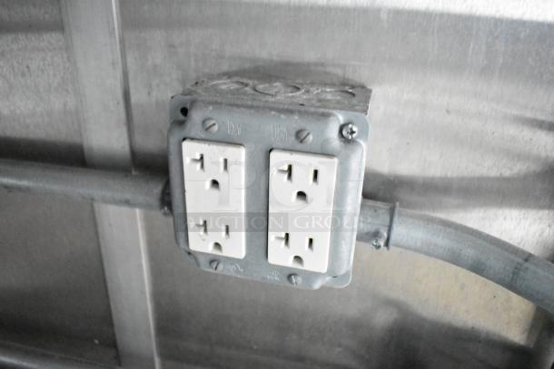 Dual electrical outlet on a mobile kitchen trailer wall, mounted in a metal junction box.