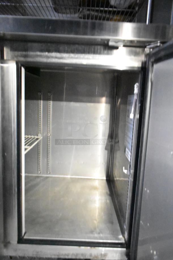 Interior view of a stainless steel cooler in a mobile kitchen trailer, showcasing shelving and storage space.