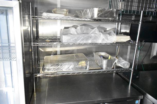 Fully outfitted mobile kitchen trailer interior with stainless steel shelving. Contains supplies and Arctic Air cooler visible.