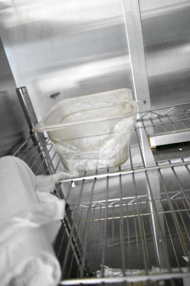 Inside of a mobile kitchen trailer with industrial-grade steel shelving, a plastic container wrapped in cling film, and stainless steel walls.