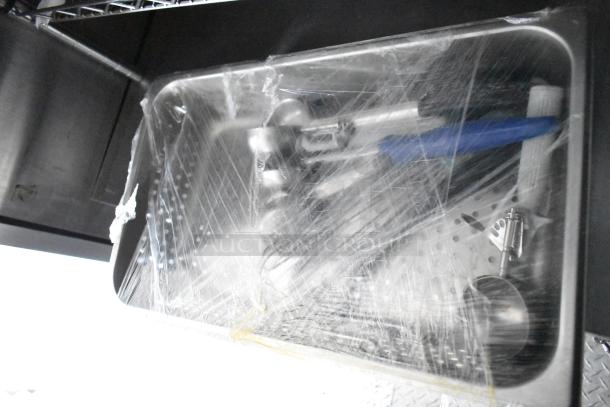 Mobile kitchen trailer sink wrapped in protective plastic film, featuring stainless steel build and integrated plumbing fixtures.