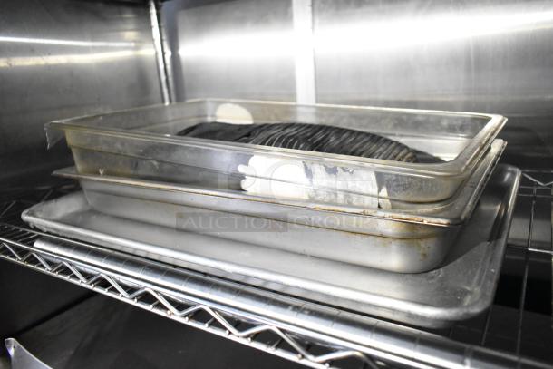Metal prep trays stacked on a stainless steel shelf, part of a mobile kitchen trailer setup.