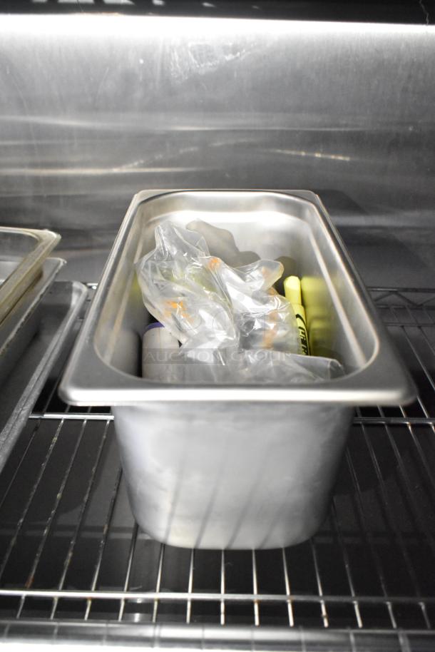 Stainless steel food pan with plastic-wrapped contents on wire shelf inside a mobile kitchen trailer.