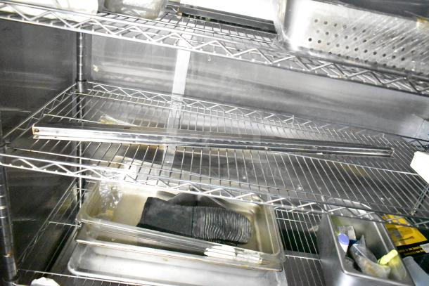 Stainless steel shelving inside a mobile kitchen trailer, containing trays and a perforated pan accessory.