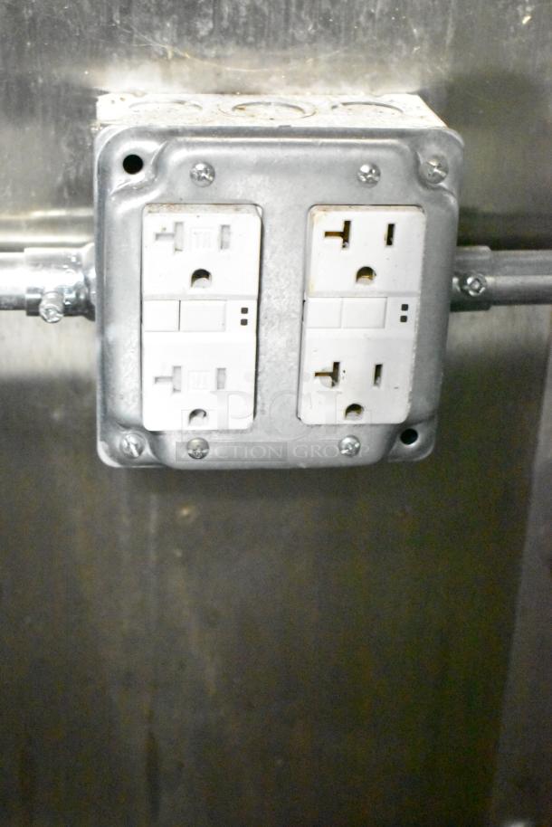 Electrical outlet in mobile kitchen trailer, showing standard dual plug setup against a stainless steel wall.