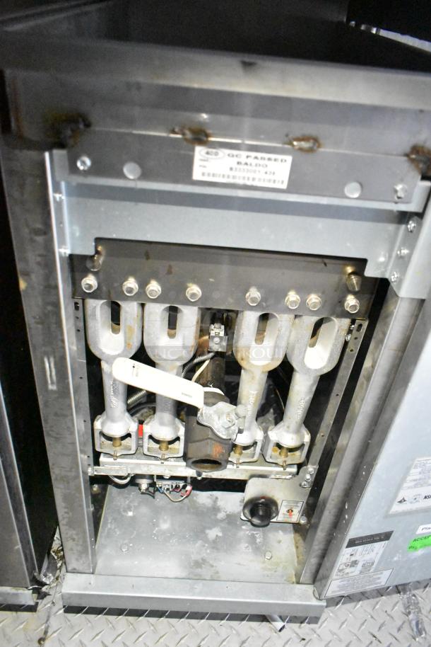 Interior view of mobile kitchen trailer equipment showing gas burner components. Labels indicate QC passed by Baldo.