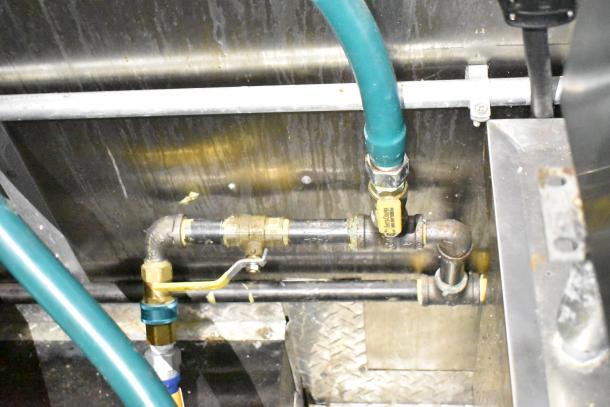 Interior piping and connections of a mobile kitchen trailer. Features visible plumbing, valves, and metal paneling.