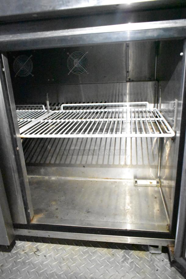 Interior view of a stainless steel Arctic Air cooler from a mobile kitchen trailer, featuring wire shelving and ventilation fans.