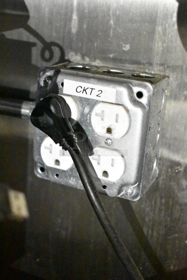 Electrical outlet labeled "CKT2" with multiple sockets in mobile kitchen trailer. Plug connected to one socket.