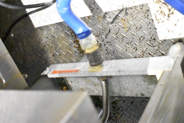 Close-up of a pipe connection inside a mobile kitchen trailer, showing a blue hose and metal fittings on a textured metal floor.