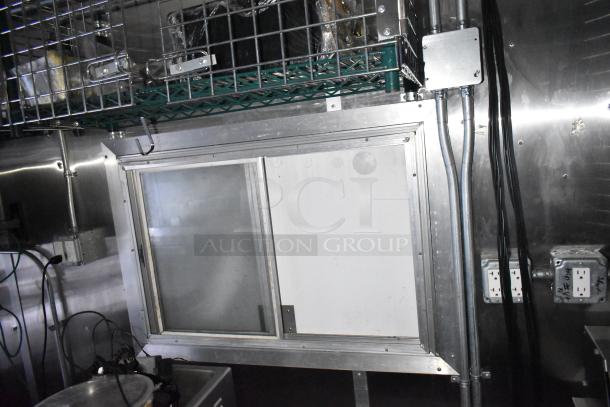 Mobile kitchen trailer interior with CaptiveAire hood, electrical outlets, and metal shelving.