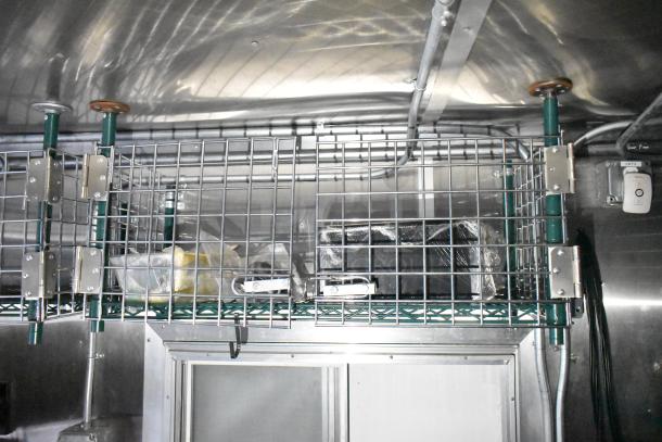Mobile kitchen trailer interior with stainless steel shelving and secure wire storage, featuring visible wiring and ventilation.