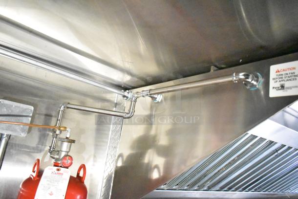 Interior of mobile kitchen trailer featuring CaptiveAire hood, stainless steel venting, visible fire suppression system, and safety labels.