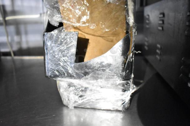 Partially packed component with plastic wrap, possibly related to mobile kitchen trailer equipment, on a metal surface.
