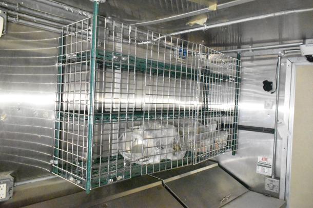 Mobile kitchen trailer interior with wire storage racks, stainless steel surfaces, and visible electrical outlets.