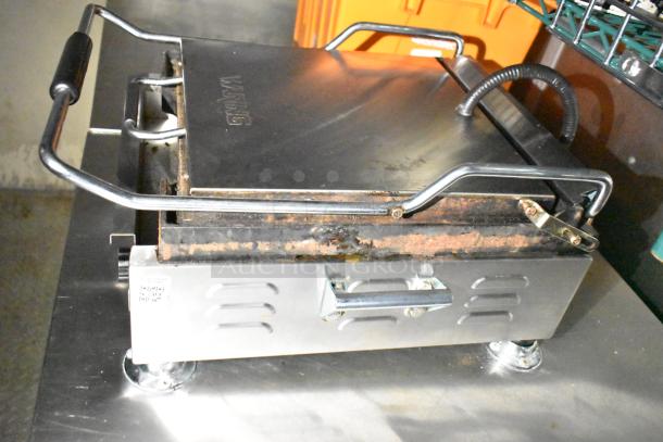 Waring panini press on stainless steel counter, showing signs of use. Features a handle and vented sides.