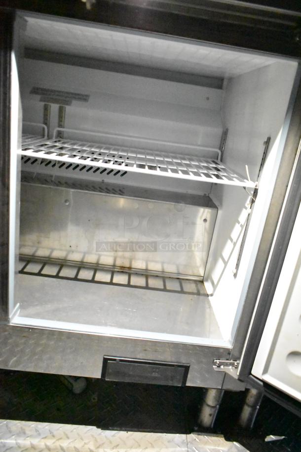 Mobile kitchen trailer interior, showing Arctic Air prep table. Features wire shelving and metallic finish, indicating durability.