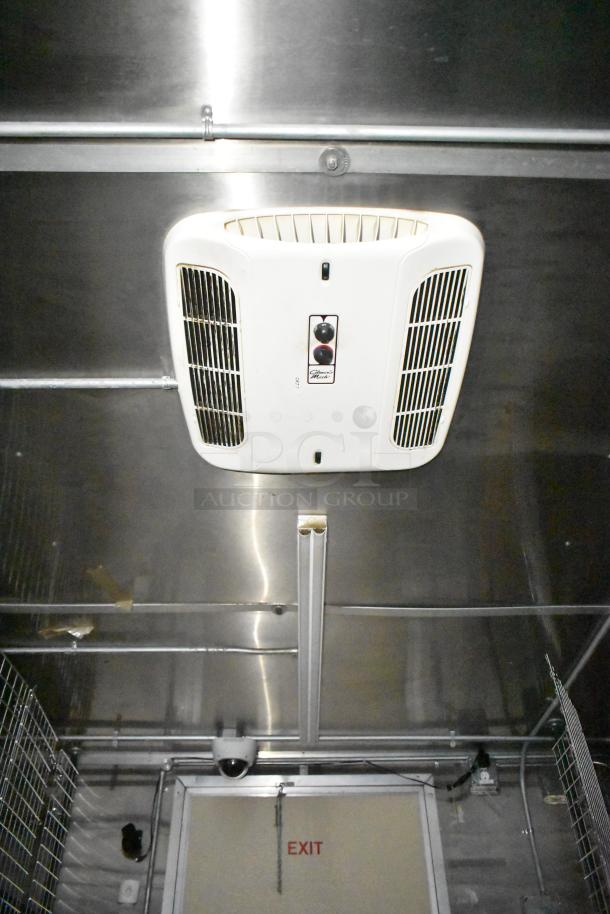 Mobile kitchen trailer interior showing ceiling air conditioning unit, stainless steel walls, and security camera above exit door.