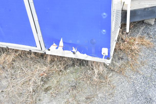 Damaged exterior of a blue mobile kitchen trailer with torn paint near the base, revealing wear and use.