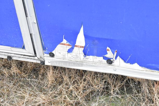 Mobile kitchen trailer with visible exterior damage, showing torn blue paneling and warning labels.