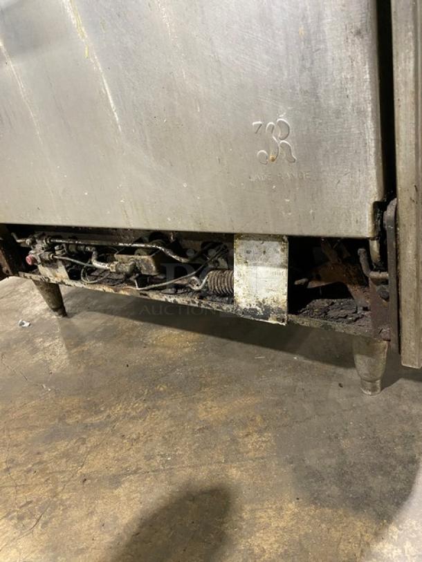 Jade Range commercial stainless steel gas-powered 4-burner char broiler range/oven combo, with backsplash and wired oven rack, on legs. Visible branding on side panel.