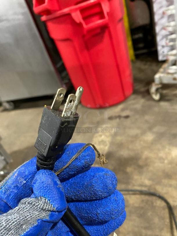 Close-up of a three-prong electrical plug held by a gloved hand, part of the Pitco fryer setup.