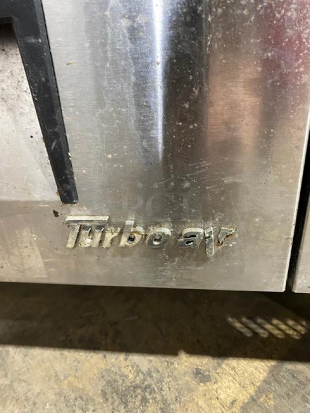 Turbo Air stainless steel 2-drawer refrigerated chef base on casters, logo visible, showing signs of wear.