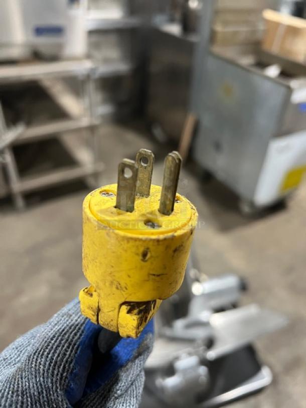 Close-up of a yellow 3-prong electrical plug for a Hobart 1612E deli meat slicer in a workshop setting.