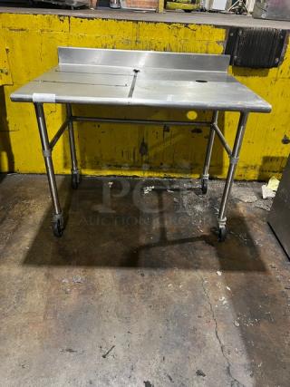 Commercial stainless steel worktop table with up-turned backsplash, on casters, used condition, ideal for kitchen use.