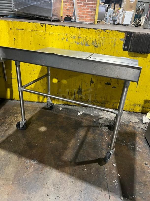 Commercial stainless steel worktop table with up-turned backsplash, on casters, used condition, ideal for restaurant or kitchen use.