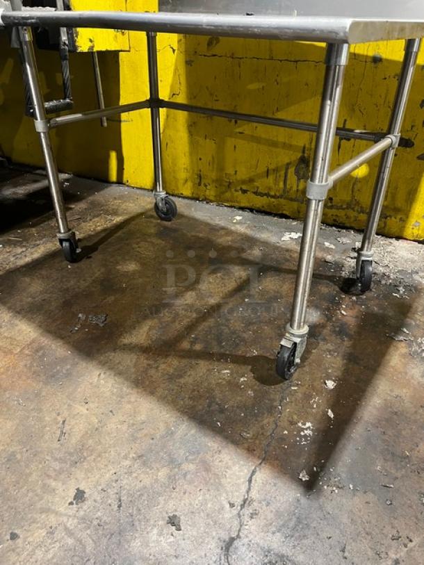 Commercial stainless steel worktop table with up-turned backsplash on casters, industrial condition.