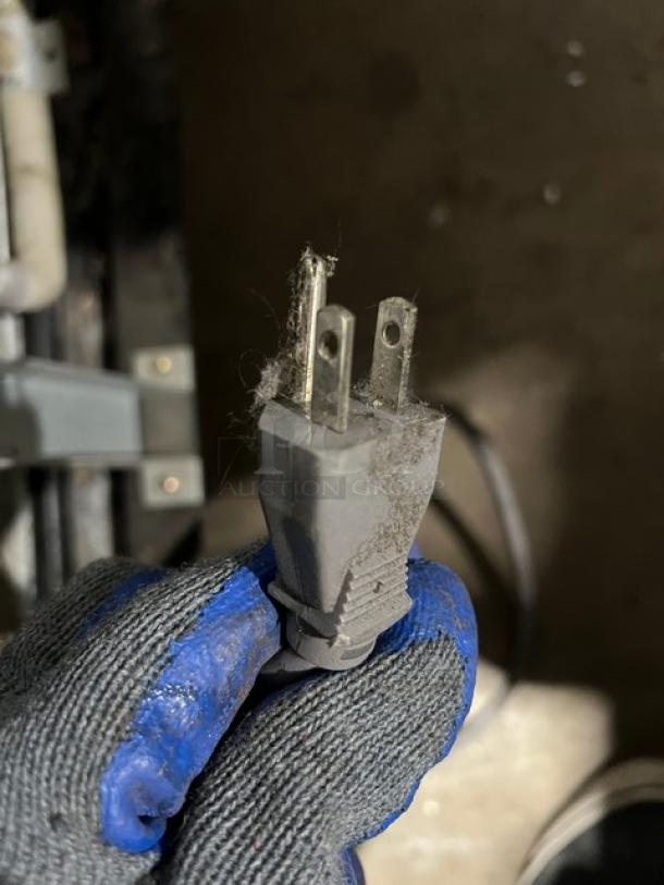 A dusty power plug held by a gloved hand. The plug is part of a Master Bilt Fusion Series Freezer, Model F49S.