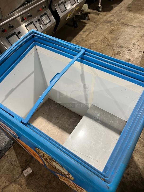 AHT RIO S100 reach-down freezer merchandiser, blue exterior, open interior, 120V, 1 phase, with model and serial markings.