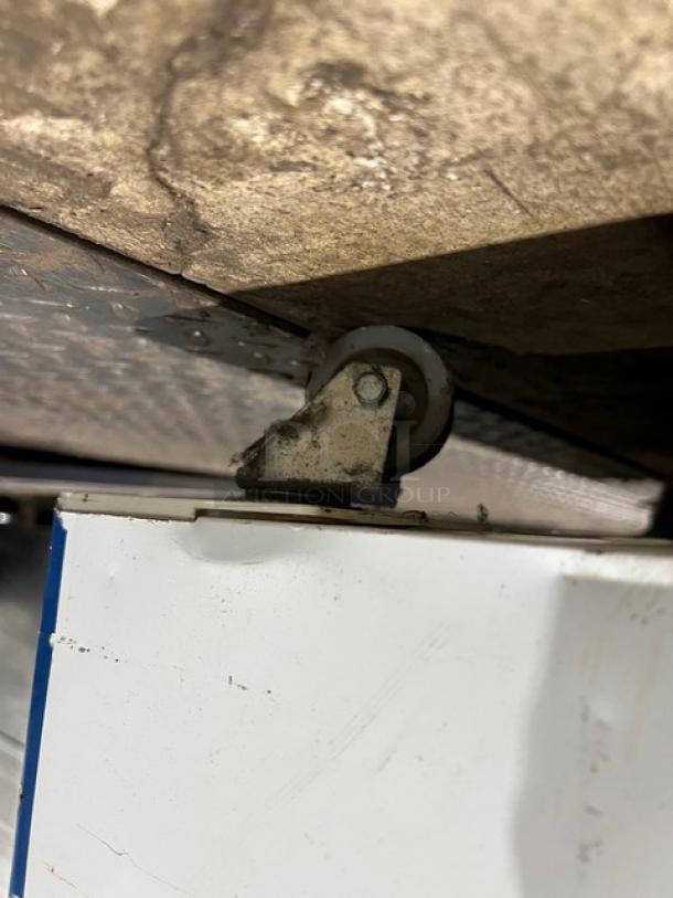 AHT RIO S100 reach down freezer wheel area, showing underside and caster. Model and serial number not visible.