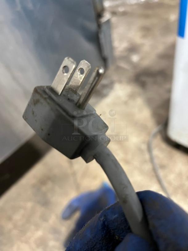 Close-up of a three-prong plug for AHT Reach Down Freezer Merchandiser, Model RIO S100, 120V, 1 Phase. Plug looks intact.