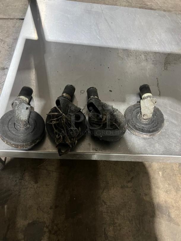 Set of four black and silver casters on a metal tray, part of a stainless steel stand for a Micro Drive pizza oven.