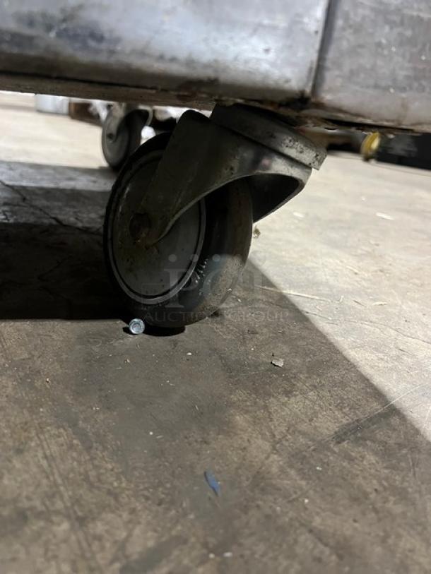 Traulsen cooler caster wheel, showing metal frame and wheel on concrete floor. Visible wear indicates used condition.