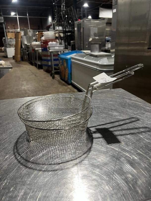 Brand new Winco FB10-M culinary basket with handle, made of durable metal mesh. Tag attached, resting on stainless surface.