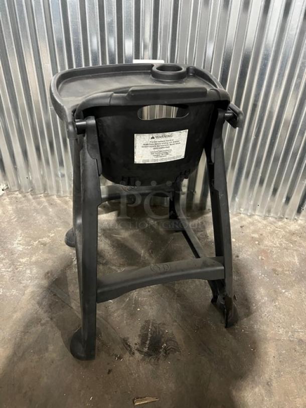 Commercial black restaurant high chair with tray, sturdy construction, visible safety label, used condition.