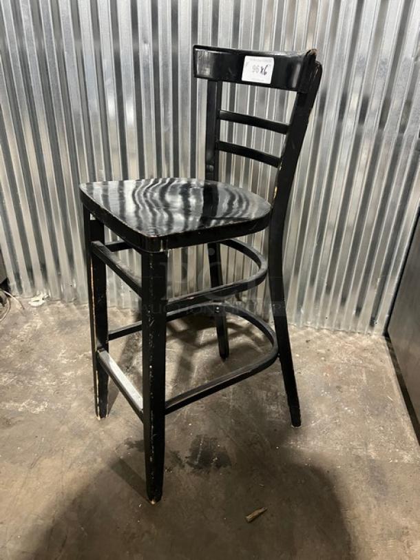 Commercial black bar-height chair with ladder back design, wooden seat, and visible wear marks. Label reads "96 KC."