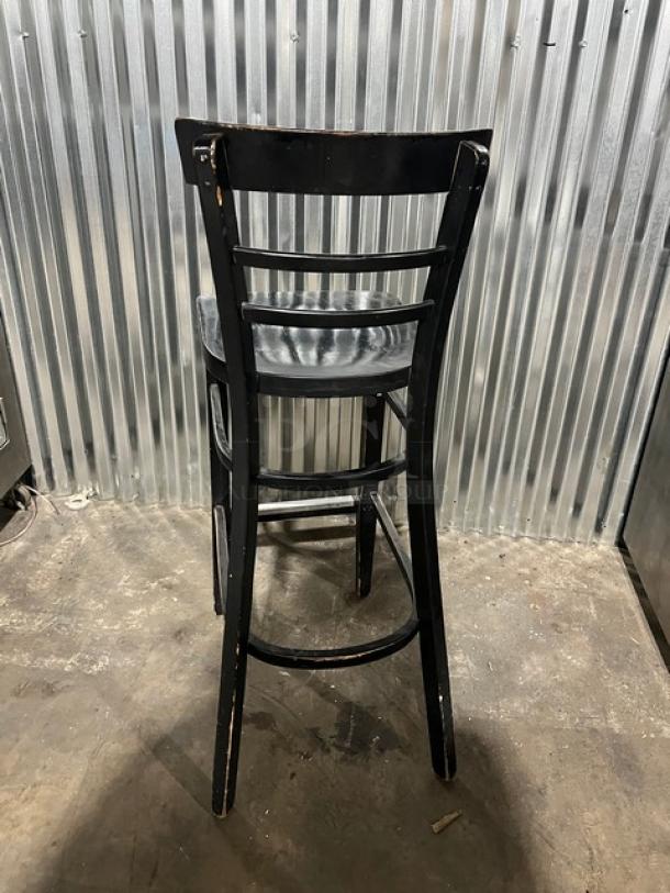 Commercial black bar-height chair with ladder back design, minor wear visible. Ideal for bar or restaurant use.