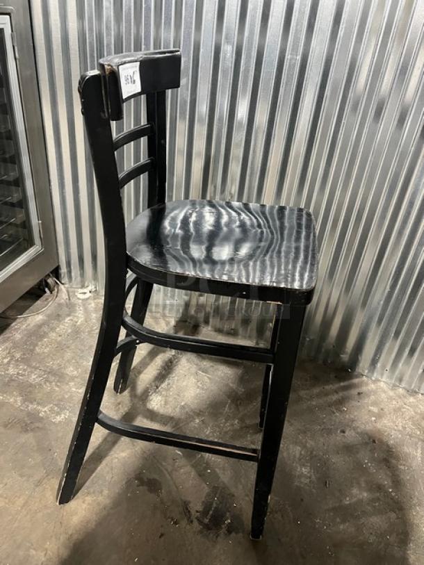 Commercial black bar-height chair, wooden frame with ladder back, in fair condition, visible wear on edges.