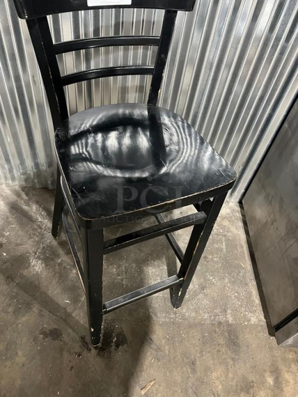 Commercial black bar-height chair with visible wear and scuffs, sturdy wooden frame, ladder back design. Suitable for bars.